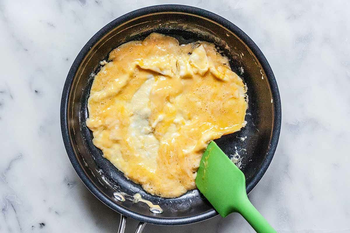 A green spatula is moving the eggs around in the omelette pan