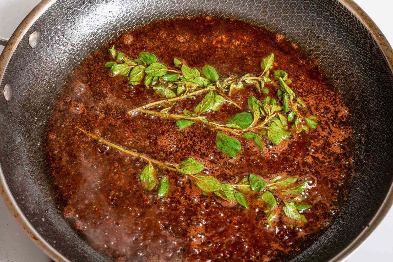 A frying pan with a sauce and sprigs of fresh herbs
