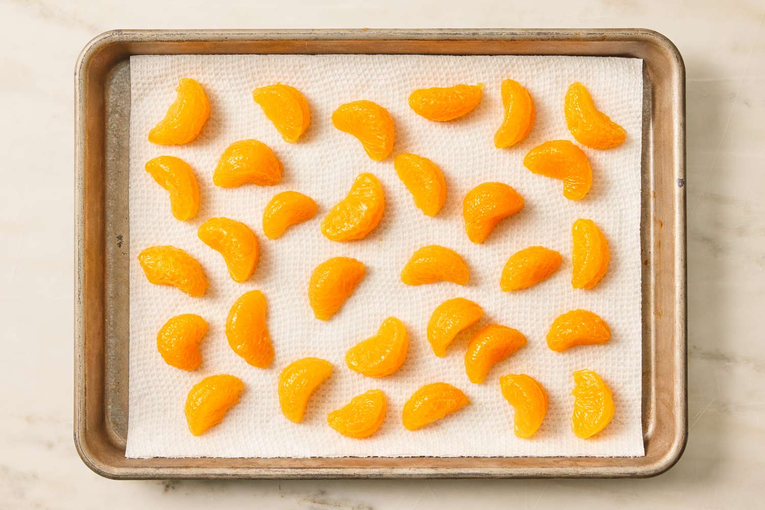 Overhead view of a baking sheet of mandarin orange slices on a paper towel for drying for Pig Pickin' Cake recipe