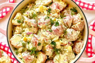 A prepared potato salad served in a pot, garnished with herbs and diced vegetables