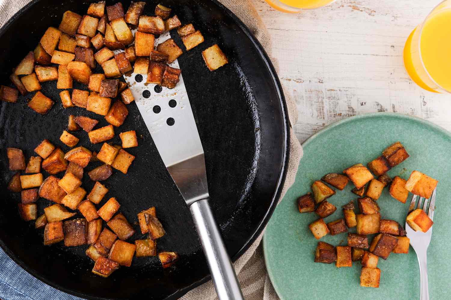 Fried potato cubes in a skillet next to a serving on a plate with a fork