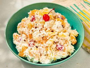 A bowl of ambrosia salad with fruit and a cherry on top