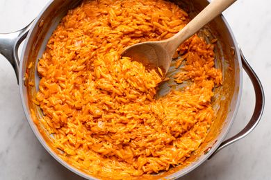 A skillet containing orzo pasta mixed with a creamy vodkabased sauce stirred with a wooden spoon