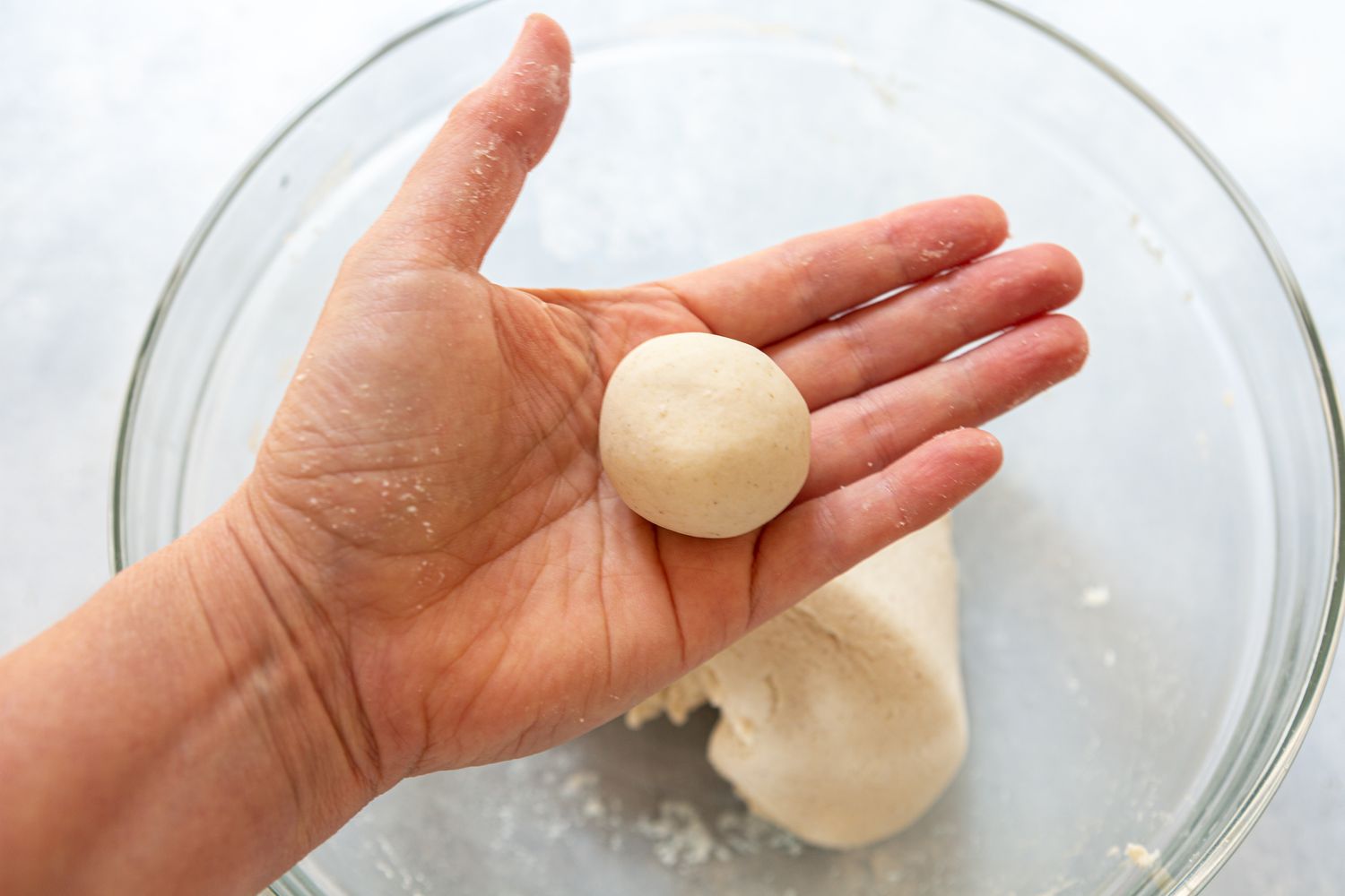 A hand holding dough that has been rolled into a ball