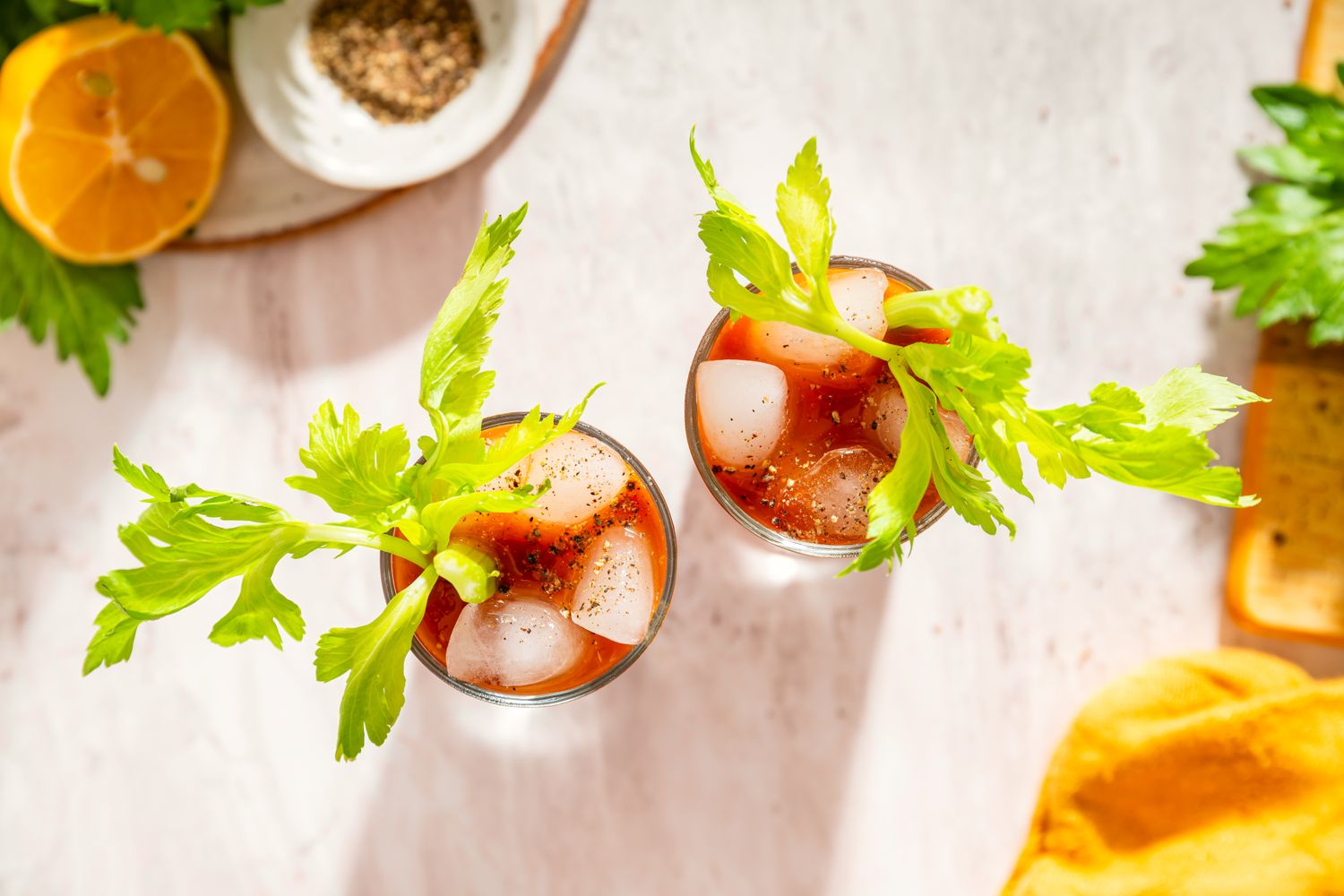 Two Bloody Mary cocktails garnished with celery sticks and served with ice on a light background