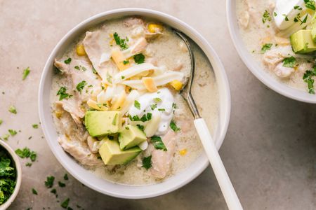 A bowl of chicken enchilada soup garnished with avocado sour cream and shredded cheese with a spoon placed in the bowl