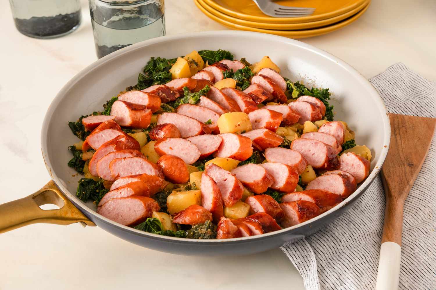 Skillet meal with sliced sausage potatoes and kale on a countertop