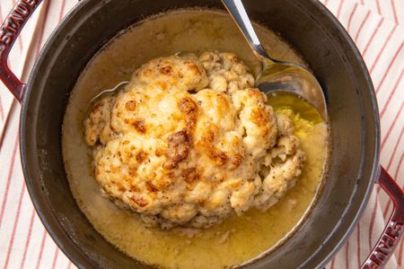 Cooked cauliflower in a pot with a spoon over liquid