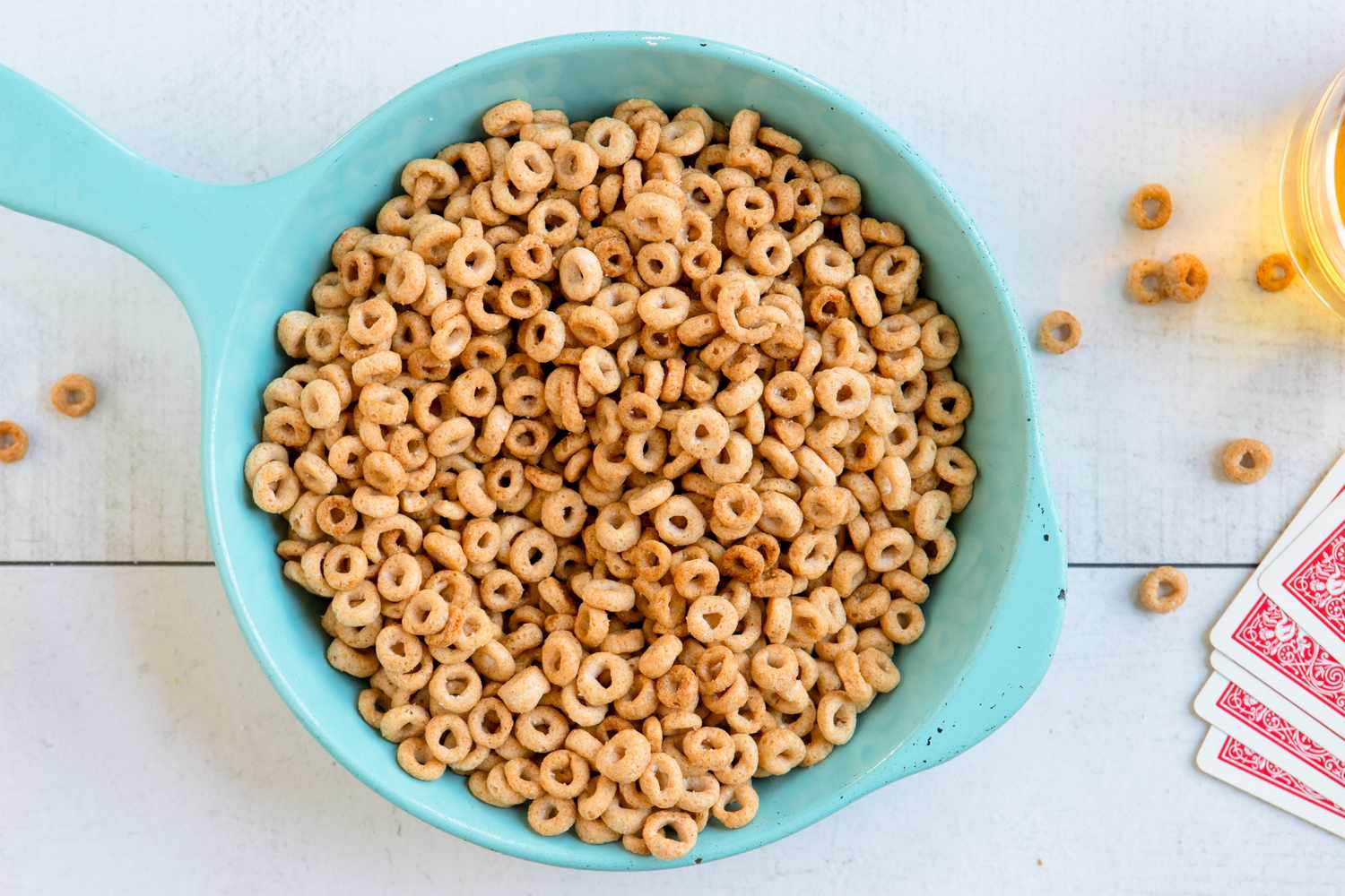 A light blue skillet filled with fried Cheerios and a glass of liquid in the background