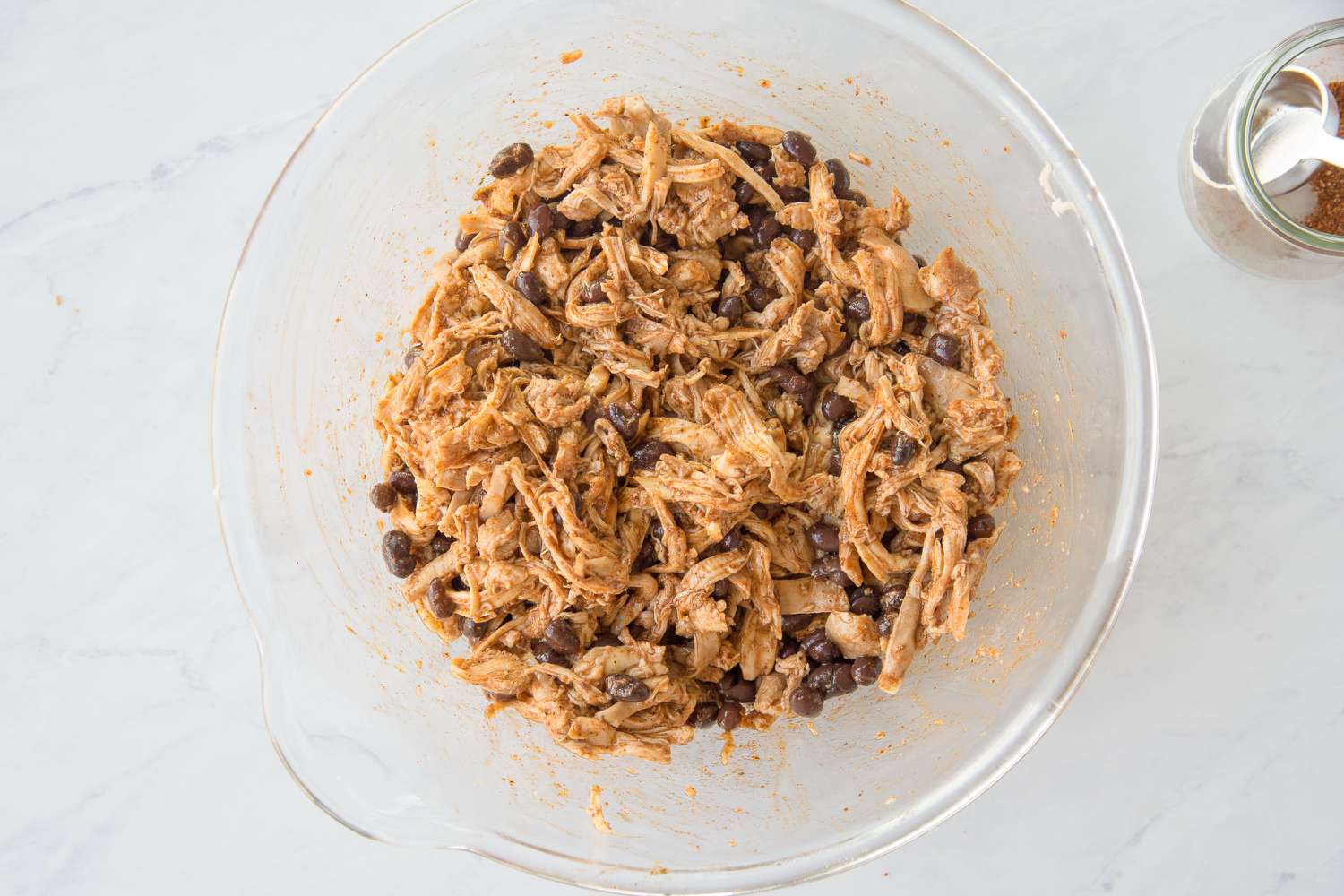 Bowl of Shredded Chicken and Beans Mixed Together With Taco Seasoning for Easy Chicken Enchilada Casserole Recipe
