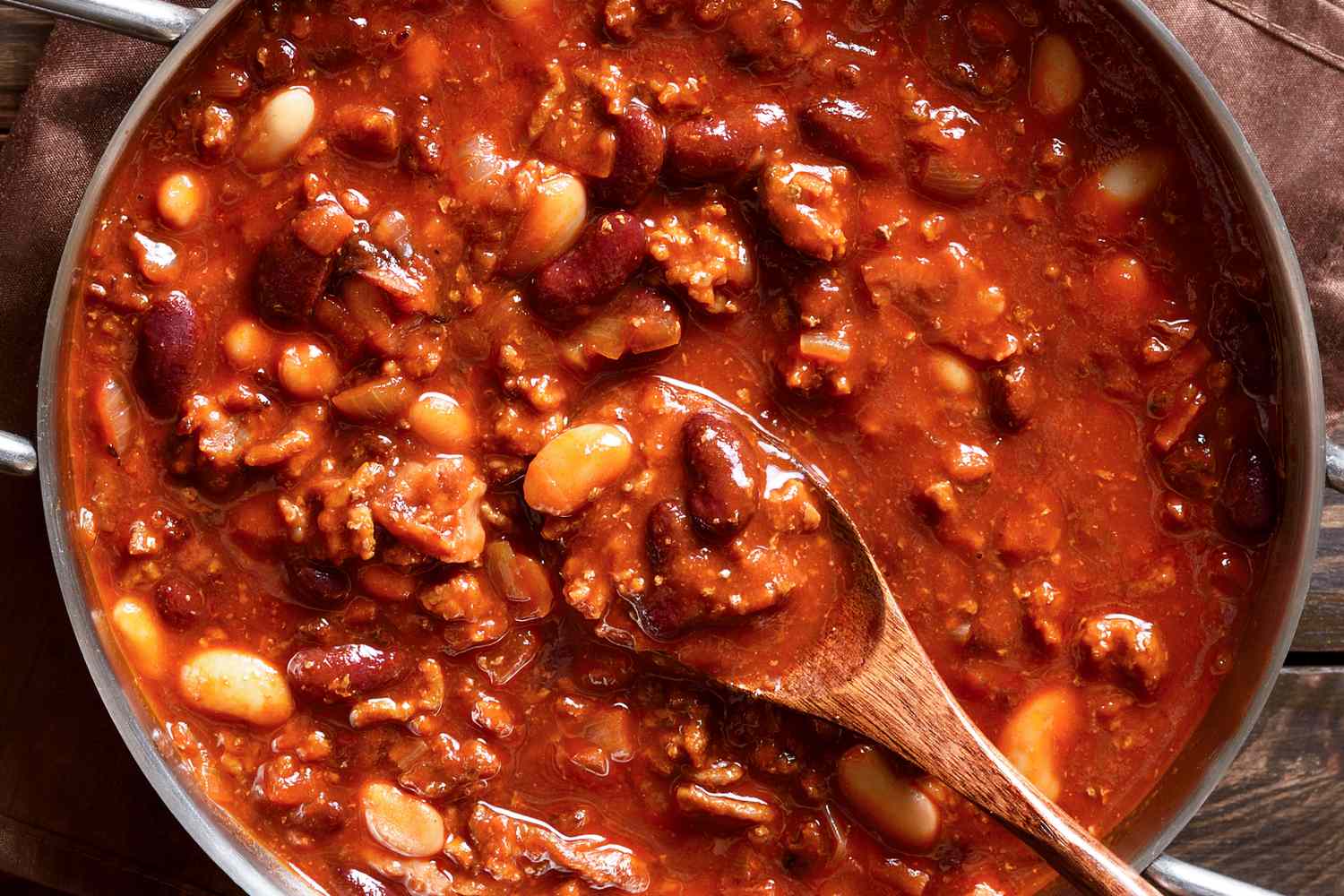 Pot of chili with beans and meat stirred with a wooden spoon