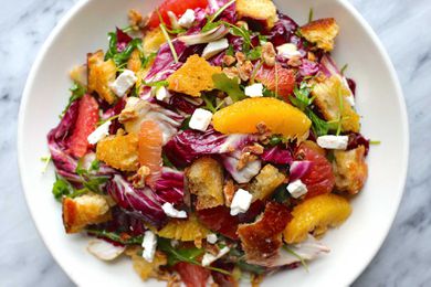 Horizontal overhead view of citrus salad on a white plate. Supremed orange and grapefruit, radicchio, croutons and feta cheese crumbles are visible.