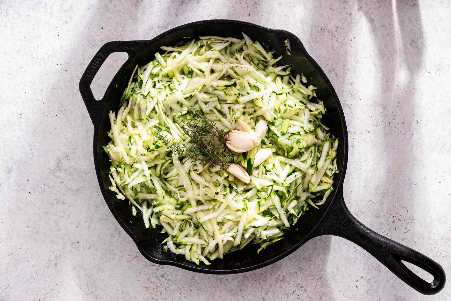 Thyme and Garlic Added to Cast Iron Skillet on Top of Shredded Zucchini for Zucchini Butter Recipe