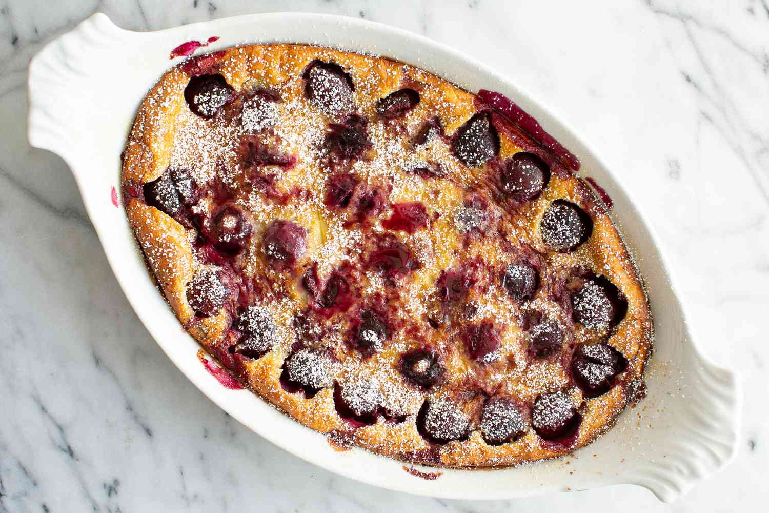 Cherry Clafoutis Dusted With Powdered Sugar in a White Baking Dish