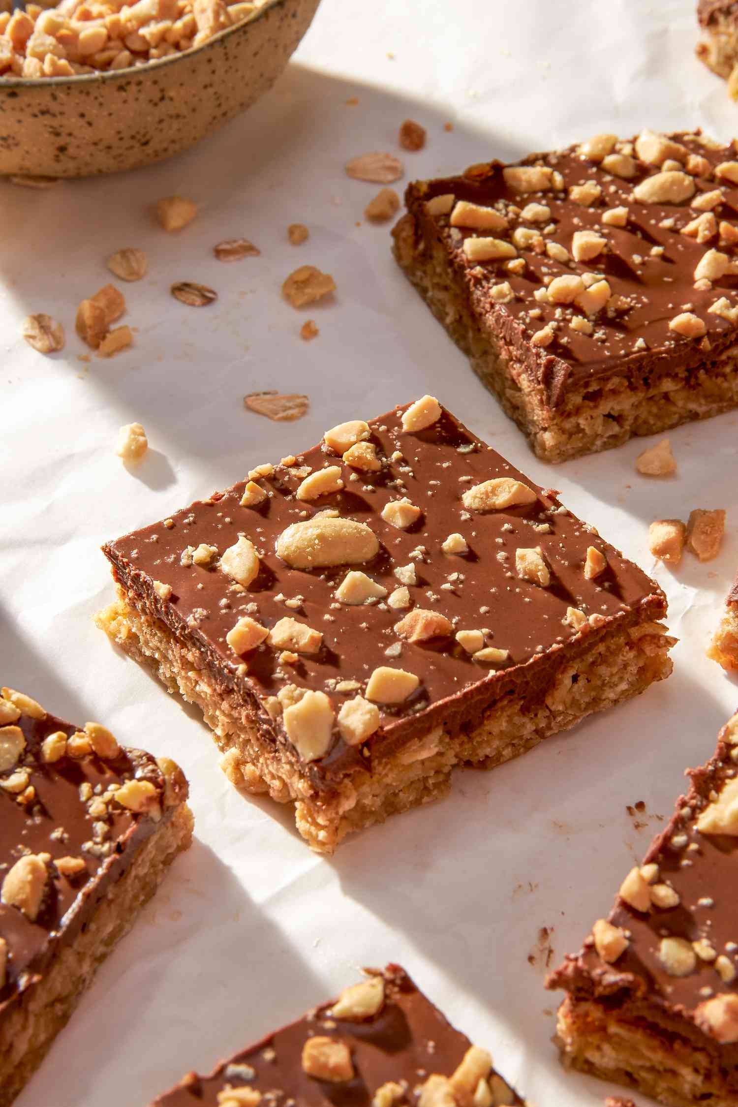 Oh Henry bars on a crinkled parchment paper with a bowl of crushed peanuts 