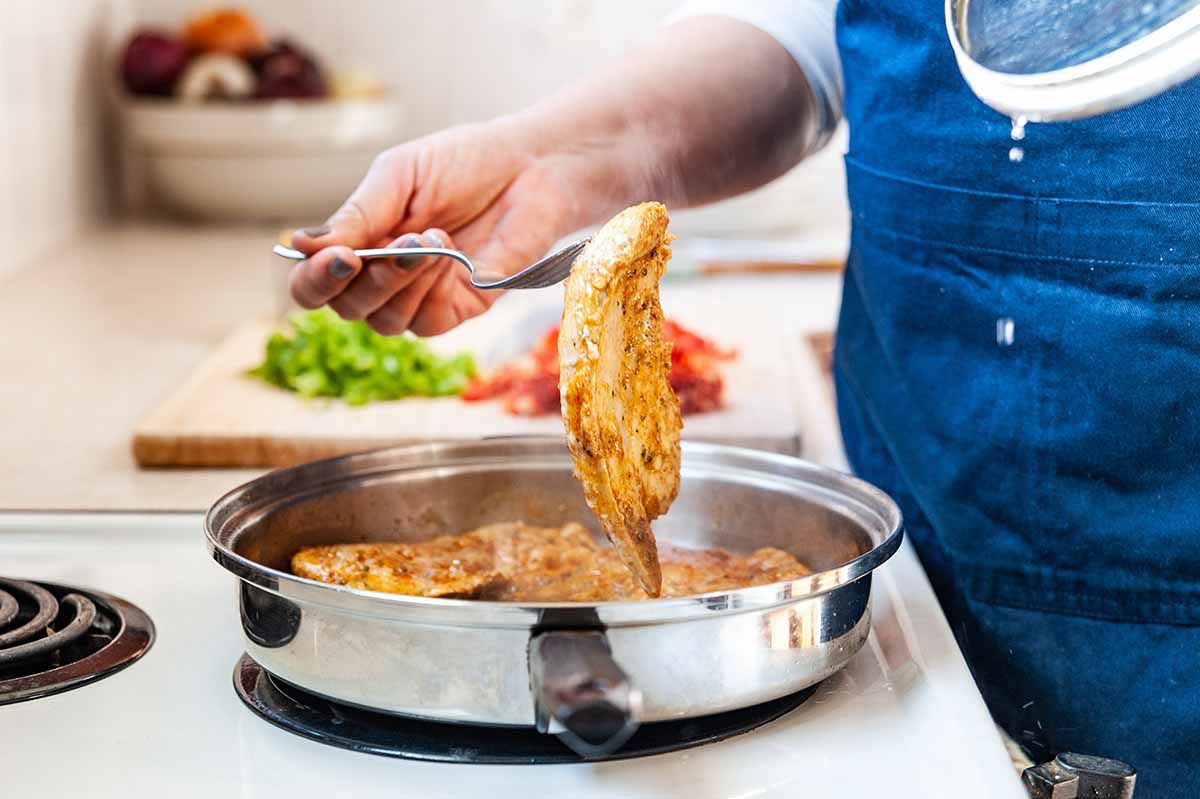 Easy Skillet Chicken - woman uses fork to pick up chicken breast and turn it over in a skillet