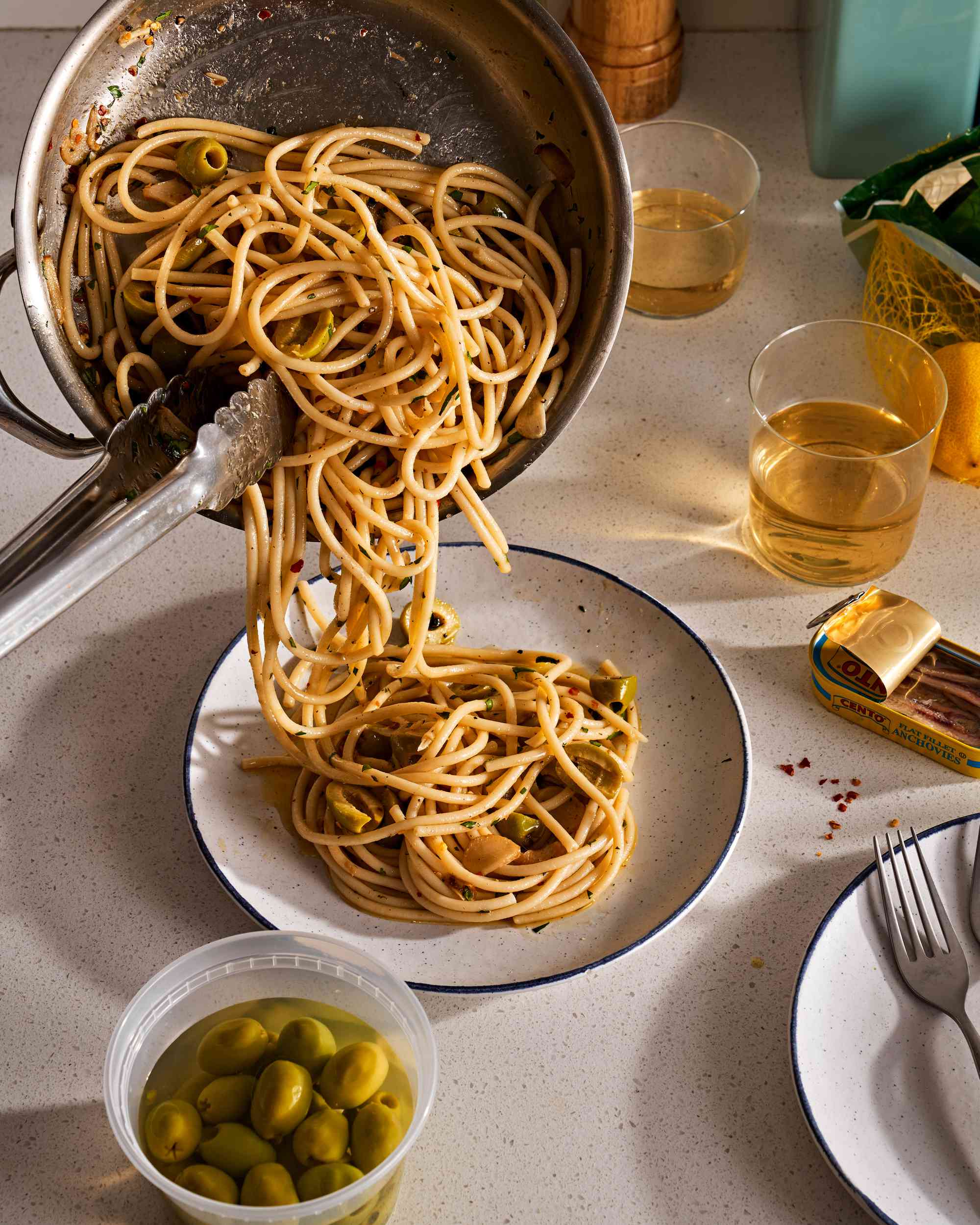 Pouring spaghetti aglio e olio from a skillet to a plate