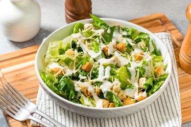 Caesar salad in a bowl with croutons and dressing on a striped towel on a wooden board