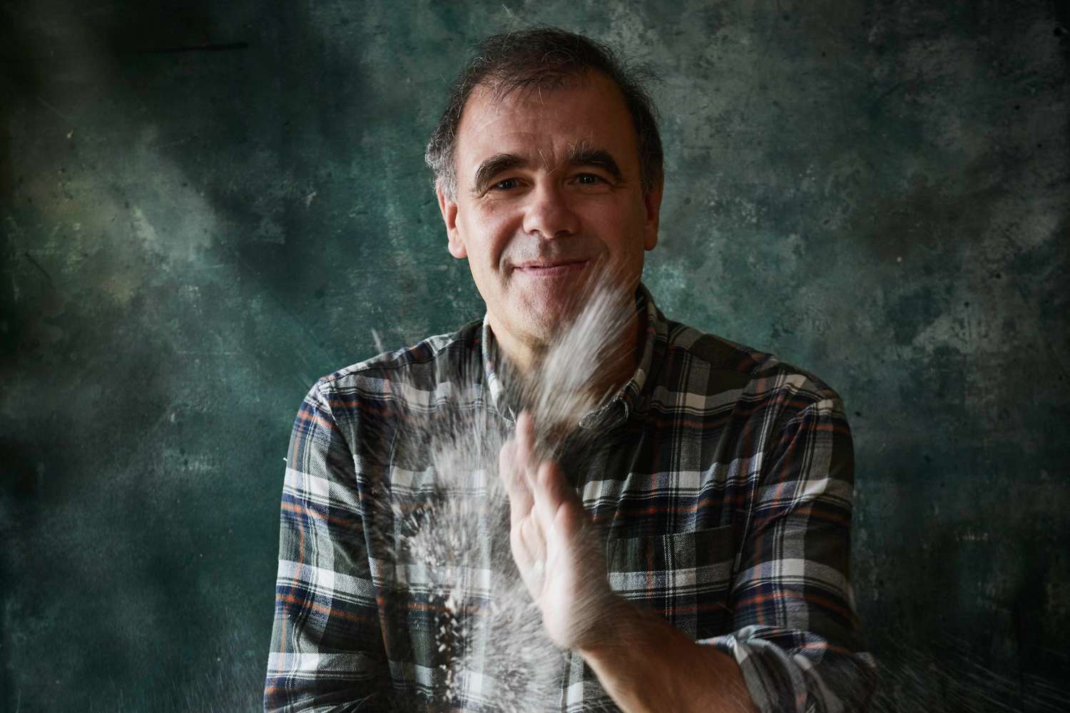 Jürgen Krauss wearing a plaid shirt smiling while flour is being scattered in the air from his hand