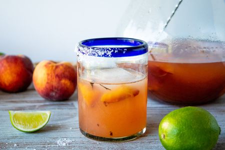 Grilled peach margarita on a table with limes and peaches.