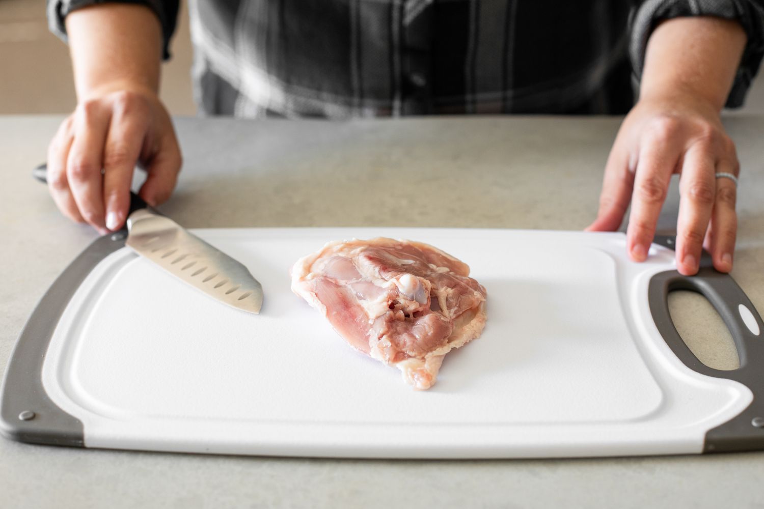 Bone in Chicken Thigh (Skin-Side Down) on a Cutting Board with a Knife in the Preparer's Hand for How to Debone Chicken Thighs