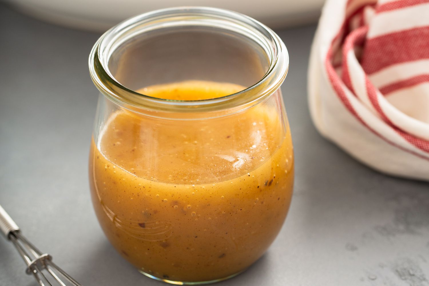 Jar of salad dressing next to a kitchen towel and whisk