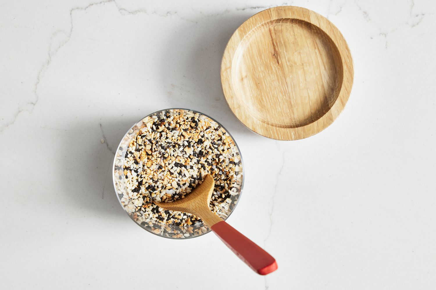 Everything Bagel Seasoning in a Glass Jar With a Wooden Spoon In It, and on the Counter Next to It, the Lid