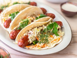 Plate of Ronto Wraps Topped With Herbs, Slaw, and Dressing, and in the Background, a Bowl of Coleslaw, a Plate With Pita Bread, and a Bowl of Dressing