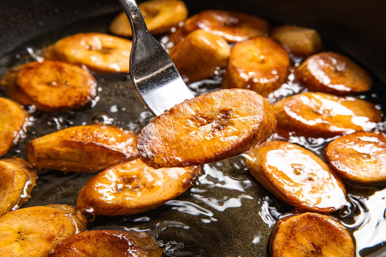 Deep Golden Colored Maduro Lifted From Frying Oil With the Rest of the Fried Plantains Using a Fork