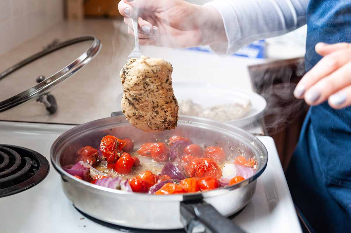 Chicken Recipe in Skillet with Italian Seasonings-woman's hand lifting a chicken breast out of a skillet with a fork
