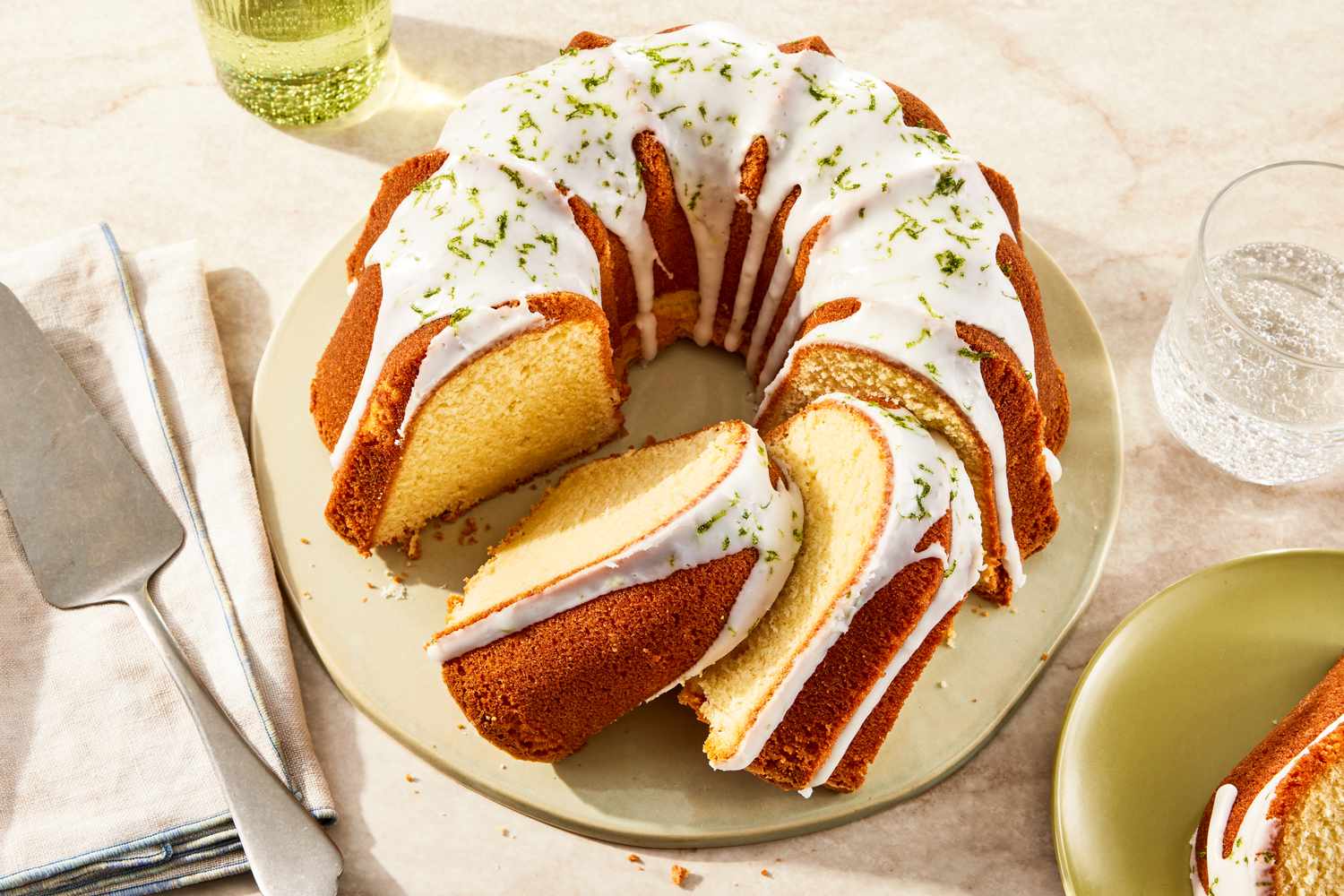 7UP bundt cake (with some slices) on a plate at a table setting with a glass of soda, a plate with a serving, and a serving spatula on a table napkin