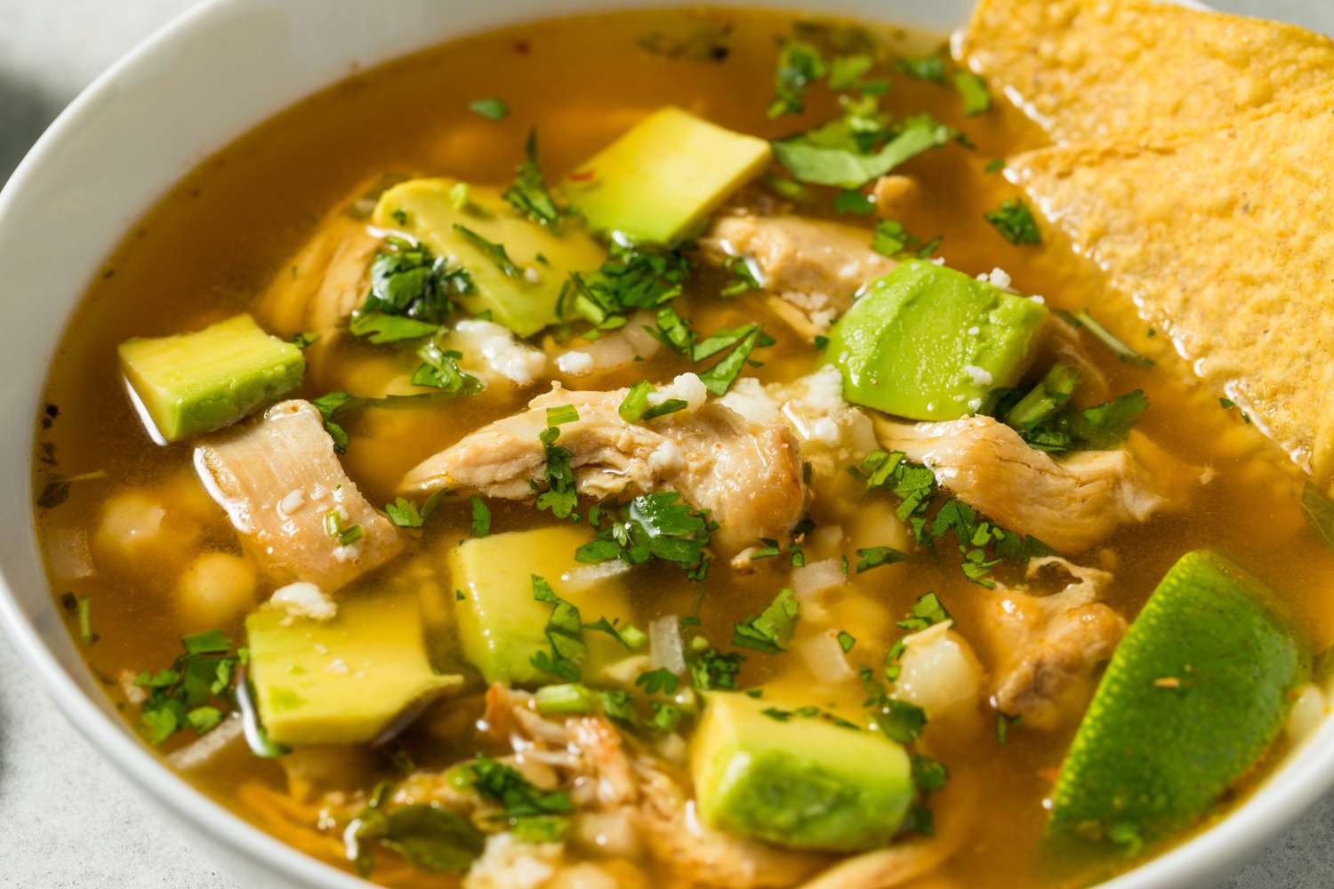 A bowl of posole soup with chicken avocado lime and tortilla chips