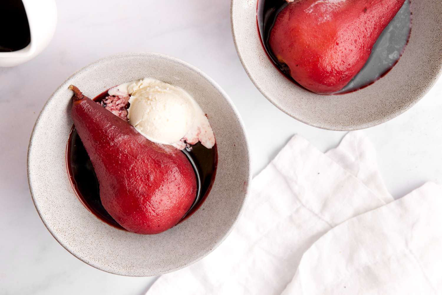 Two poached pears in small white bowls with ice cream.