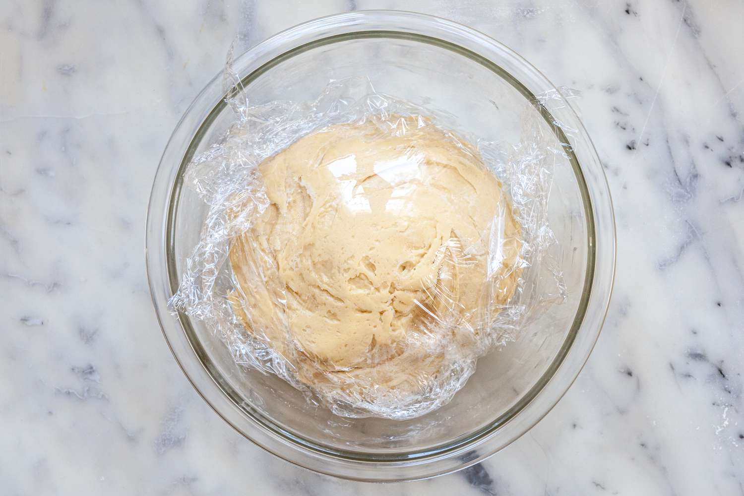 Dough covered in plastic wrap to make homemade brioche buns.