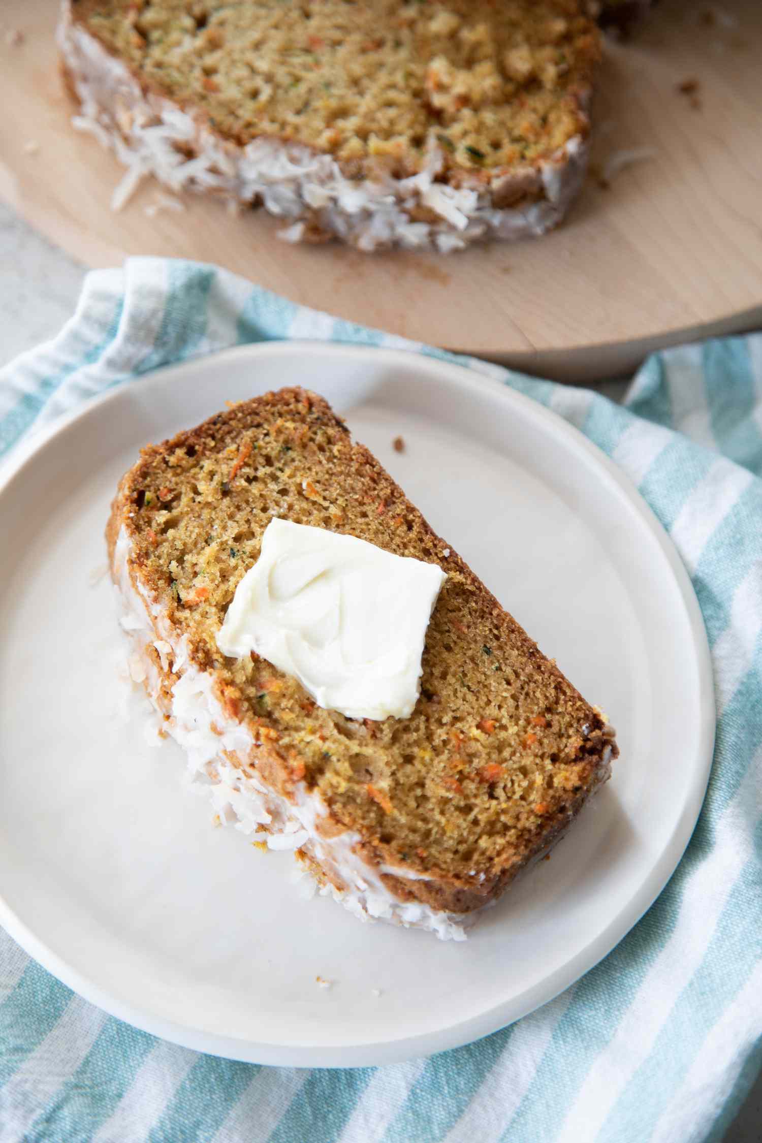 Slice of Zucchini Carrot Bread with Butter on a Plate Next to Board with More Bread
