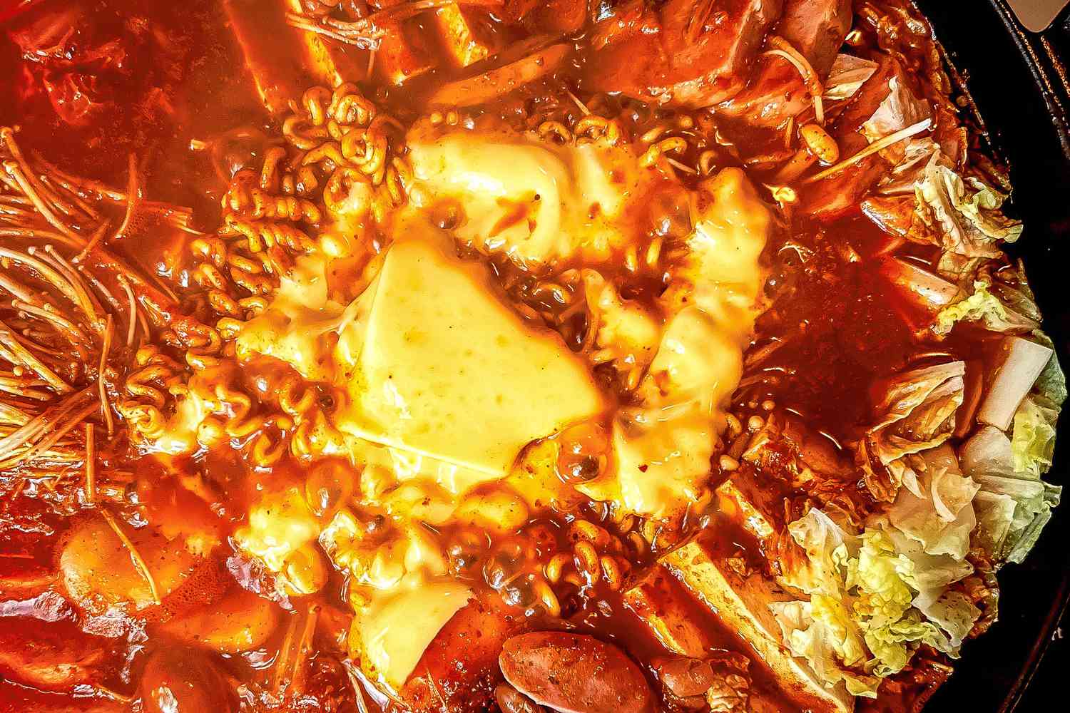 Close-up: budae jjigae (army base stew) topped with a piece of melted cheese in a large pot