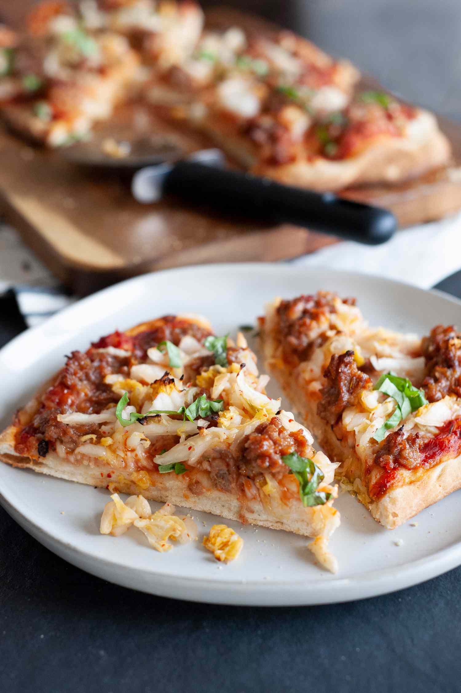 Kimchi and sausage pizza on white plate. 