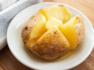 Angled view of a small white plate with a baked potato sliced in quarters and topped with butter