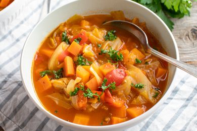 Healthy vegetarian and detox soup with fresh vegetables and cabbage. Served in a bowl with spoon on wooden table