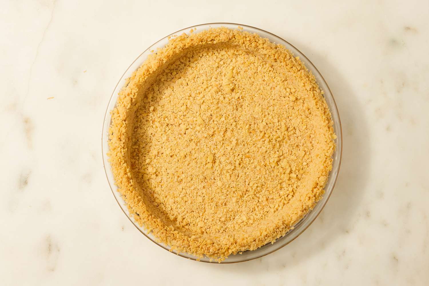 Overhead view of the crust for Atlantic Beach Pie recipe in a glass pie dish on a marble countertop