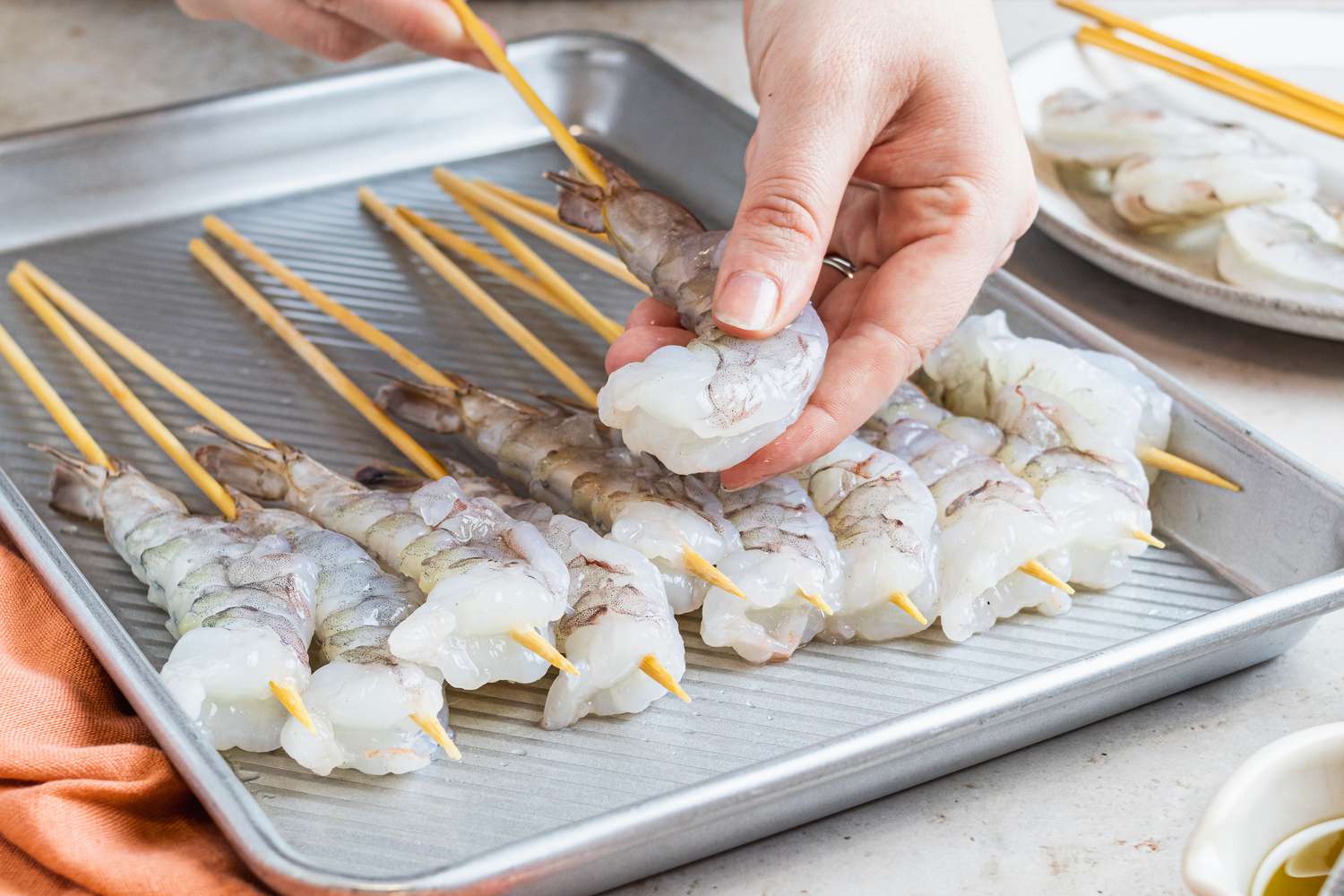 A person putting shrimp on a stick and setting on a bakings sheet.