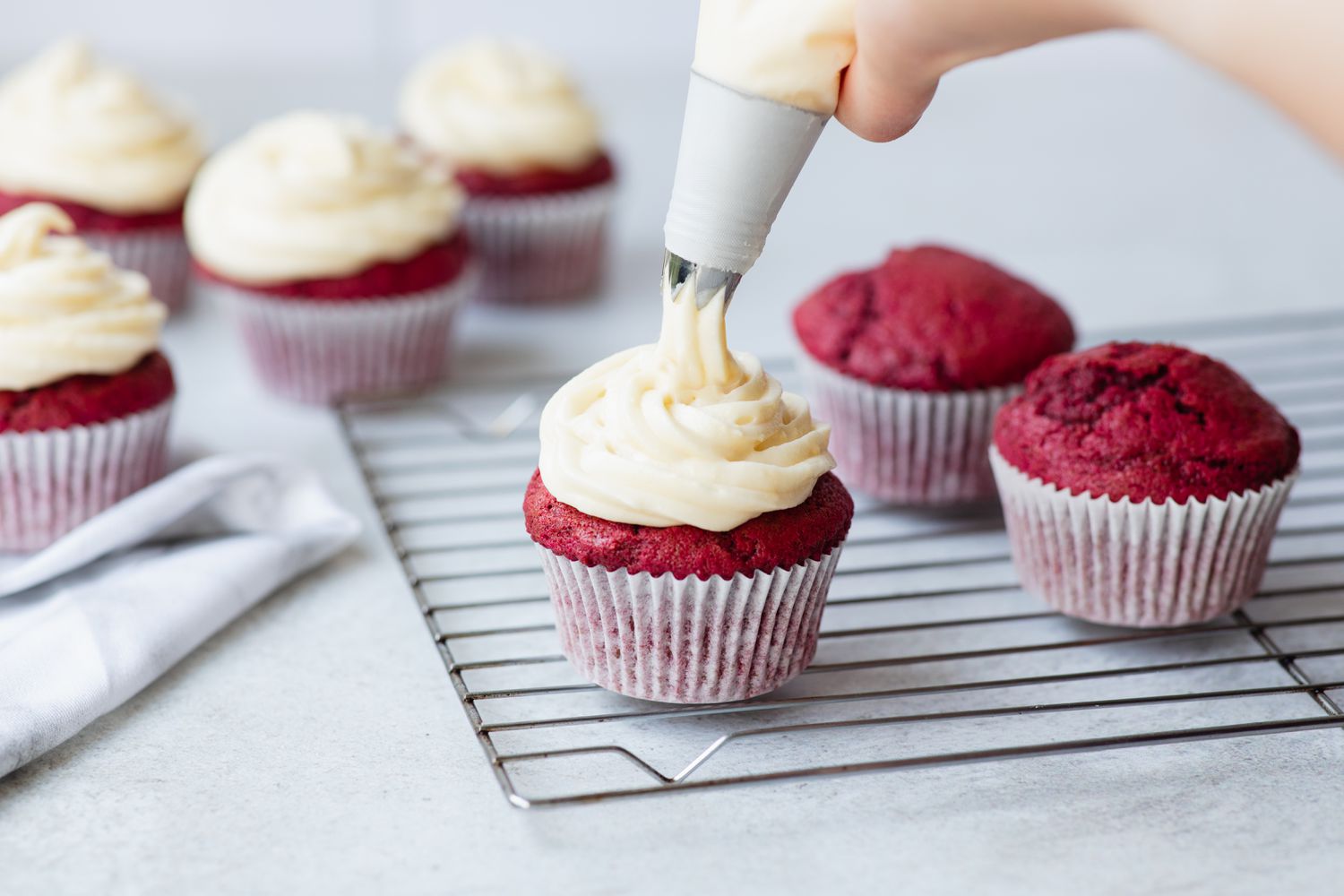 Piping cream cheese frosting on red velvet cupcakes.