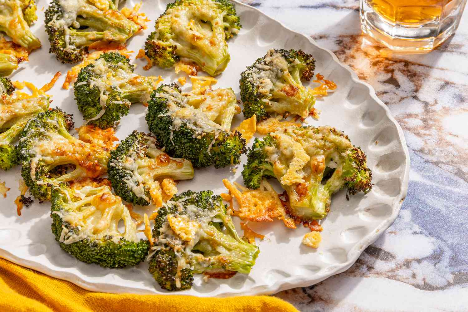 crispy parmesan broccoli on a platter next to a table napkin and a drink in a glass