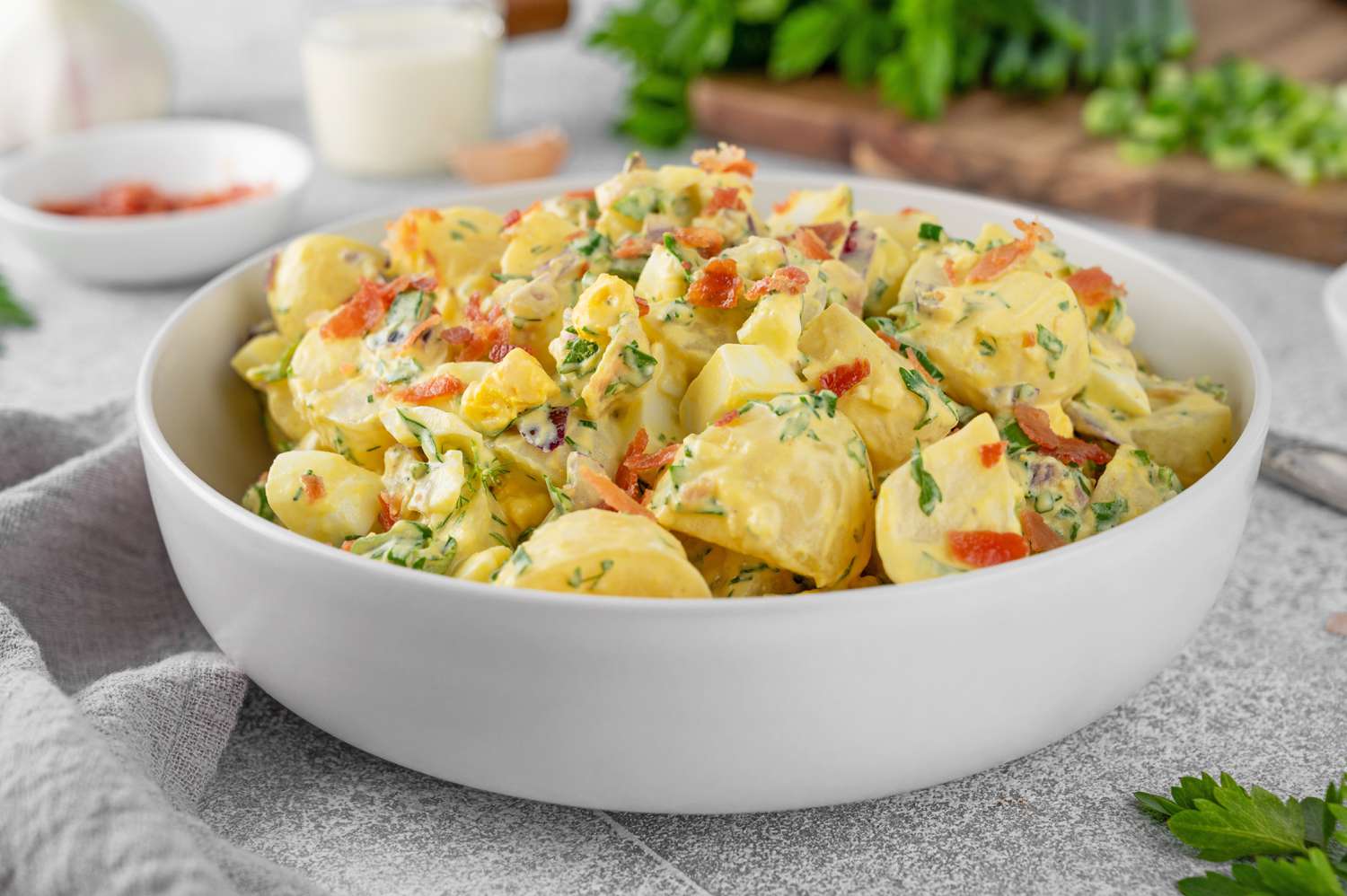 A bowl filled with loaded potato salad, garnished with bacon and herbs
