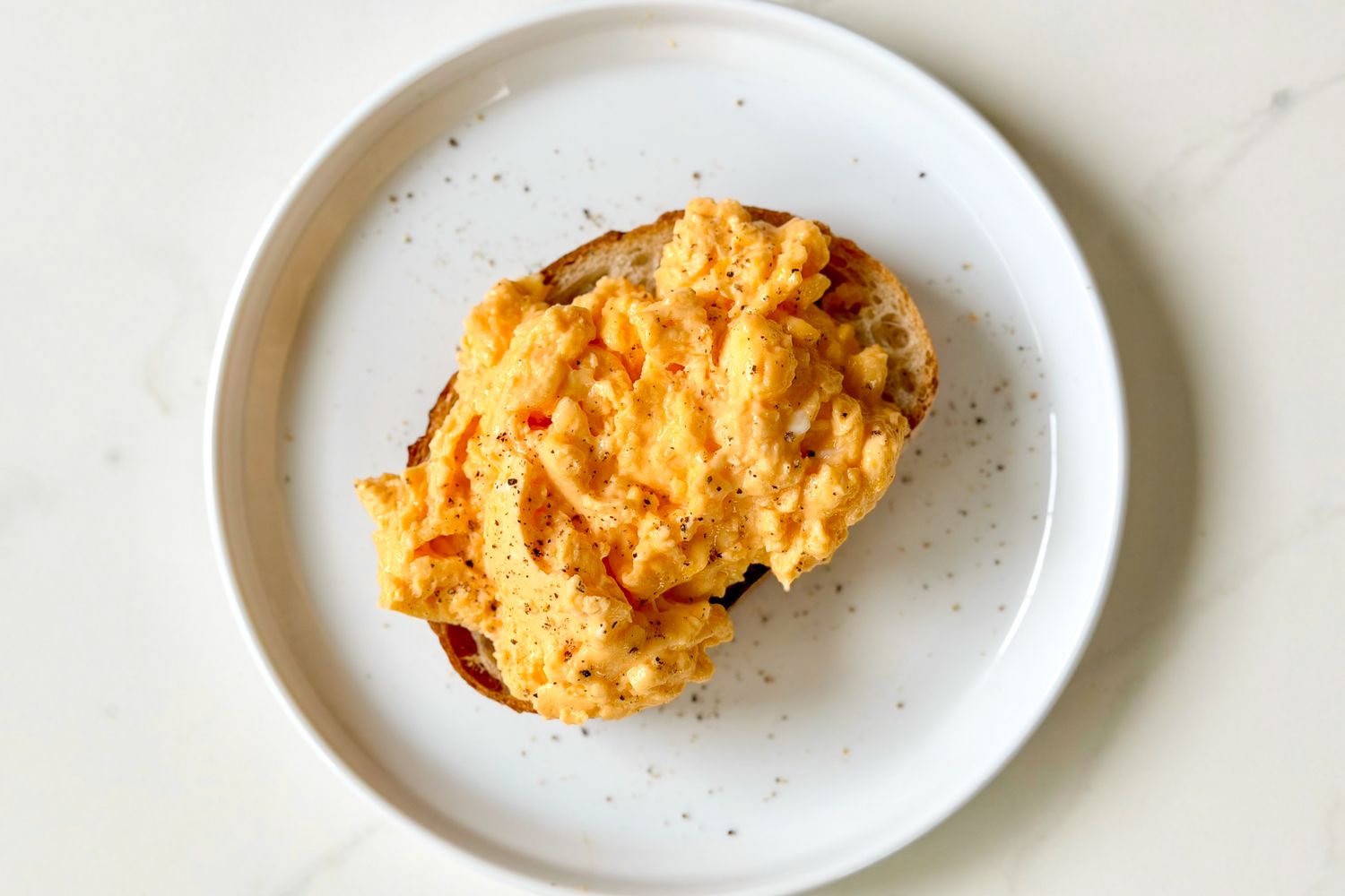 Scrambled eggs served on a piece of toasted bread presented on a white plate