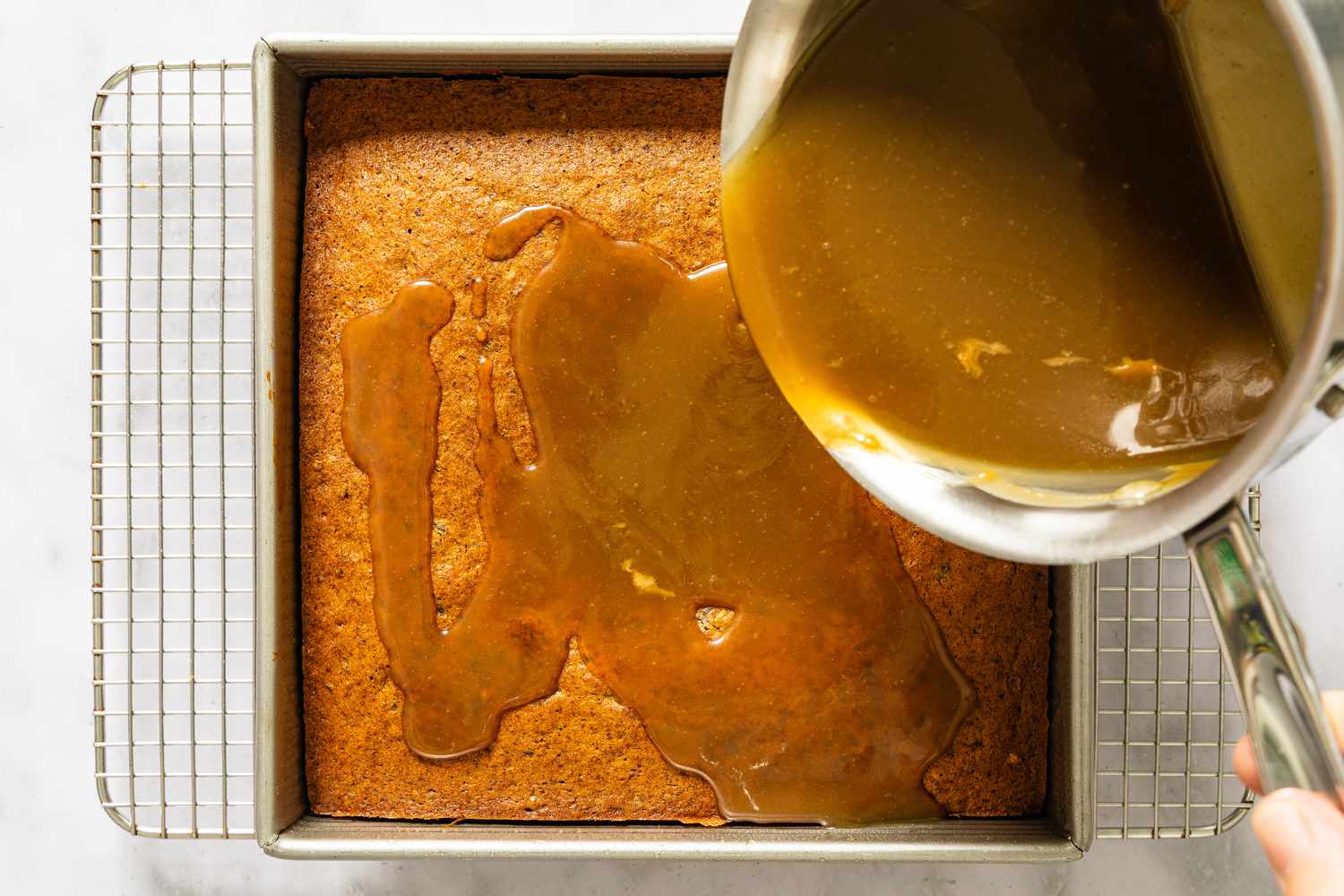 A baking dish with a dessert being topped with sauce from a saucepan