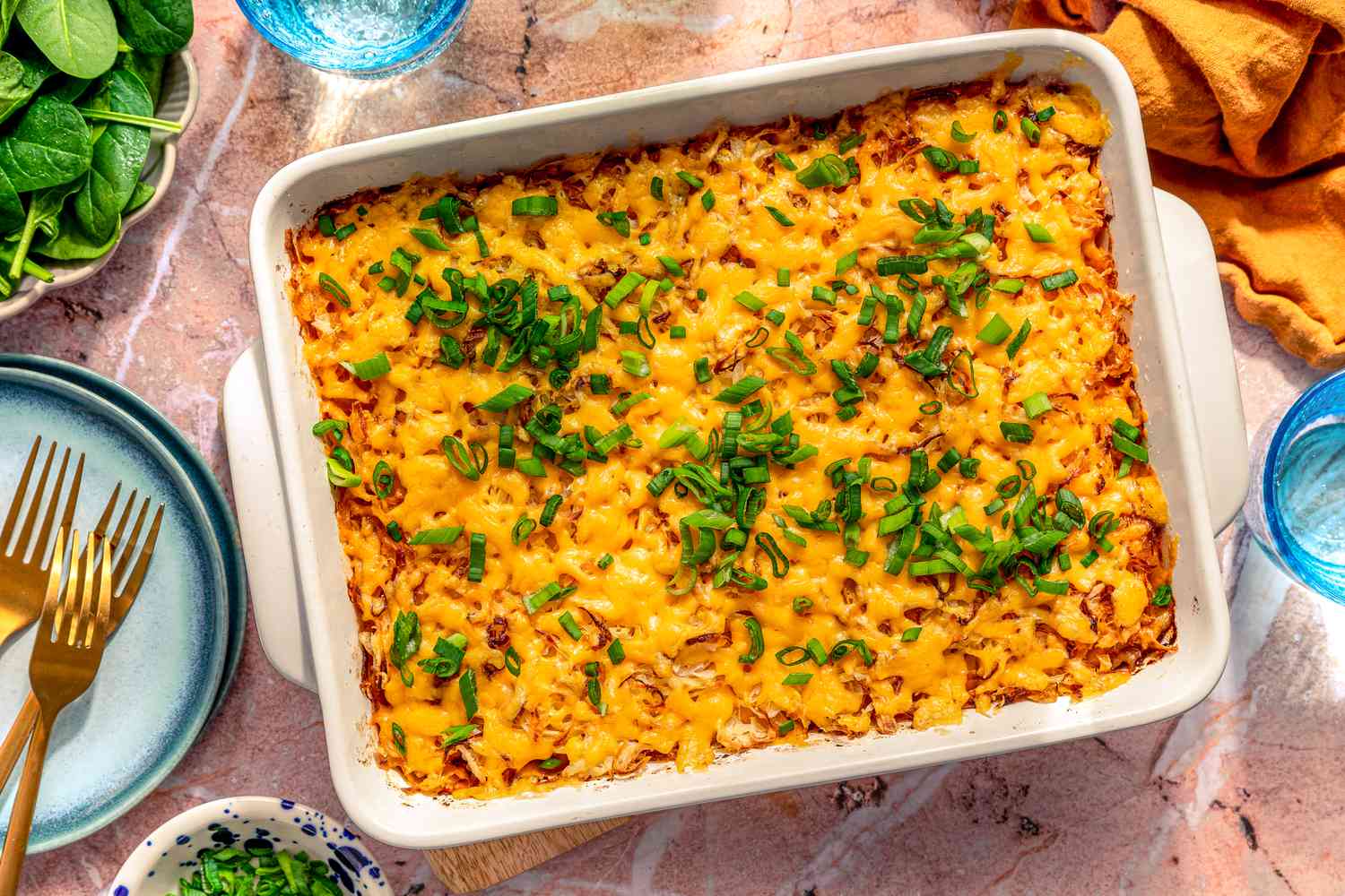 shipwreck casserole in a casserole dish at a table setting with a bowl of scallions, plate, and glass of water 