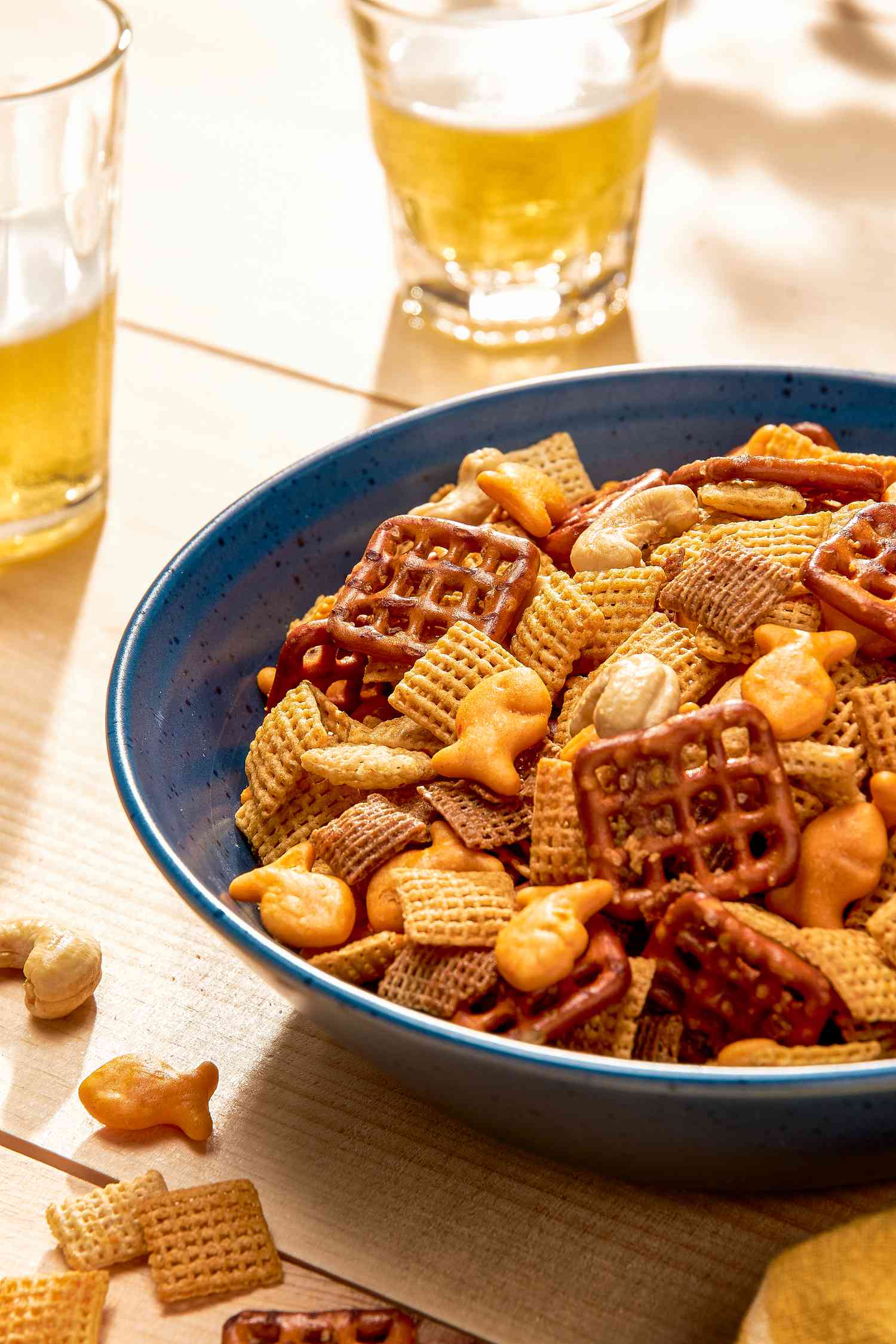 Sweet and spicy chex mix in a bowl at a table setting with two glasses of beer and a yellow kitchen towel