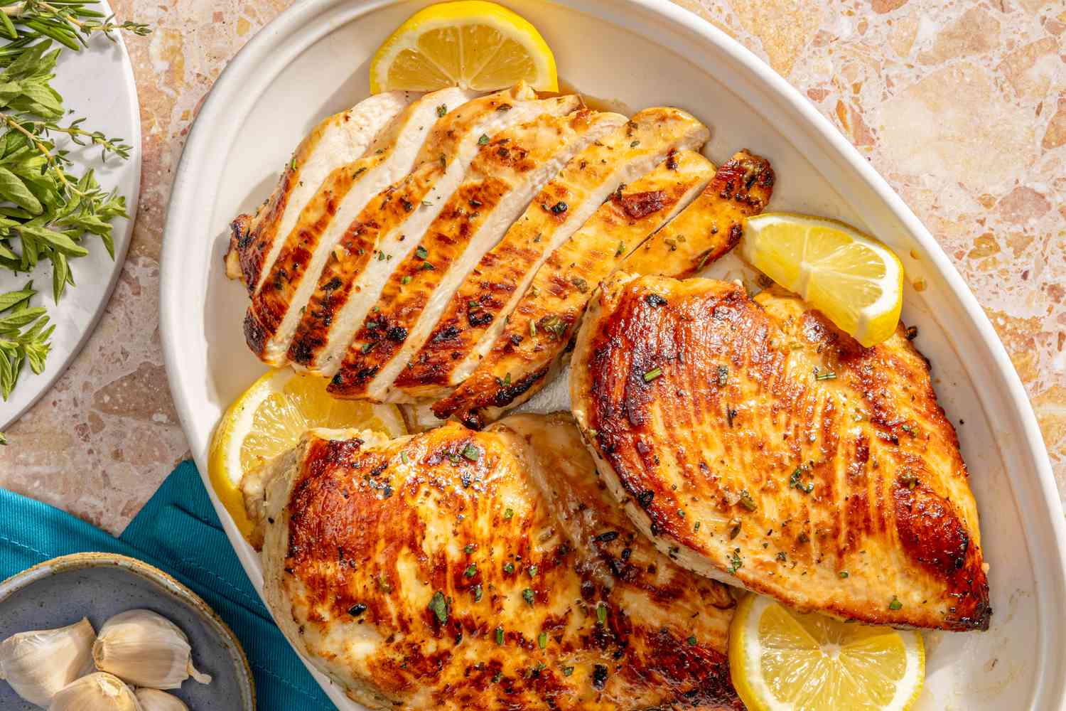 Marinated chicken breasts on a white platter with lemon slices