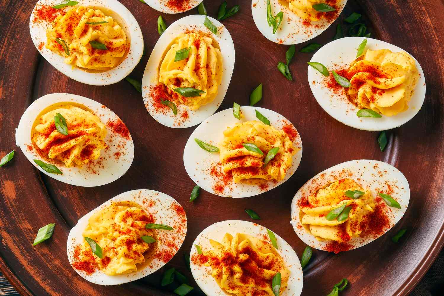 Deviled eggs garnished with paprika and green herbs arranged on a platter
